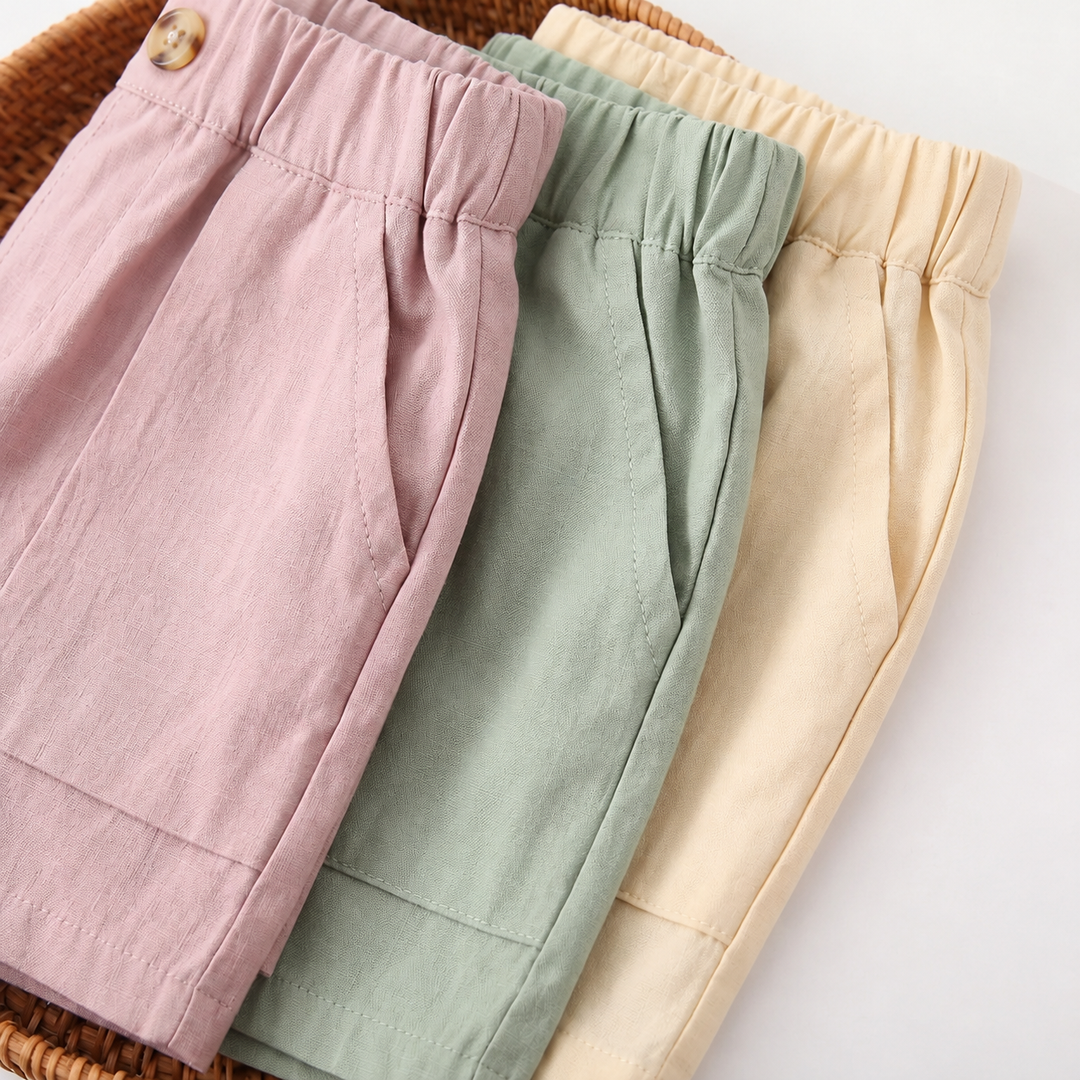 Close-up of gathered elastic waistbands and pocket stitching on pink, sage green, and light beige shorts.