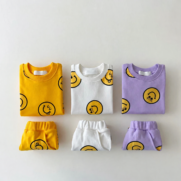 Folded yellow, white and purple smiley-print T-shirts with matching shorts arranged below