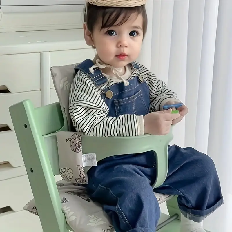 Child seated with a gray tiger-and-leaf cushion in a mint-green high chair