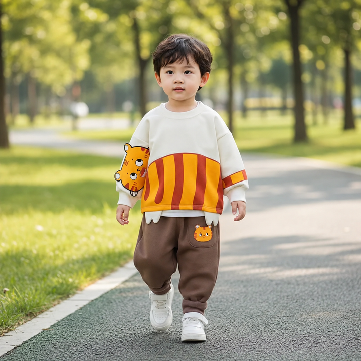Child wearing a cream tiger sweater and brown pants on a park path.