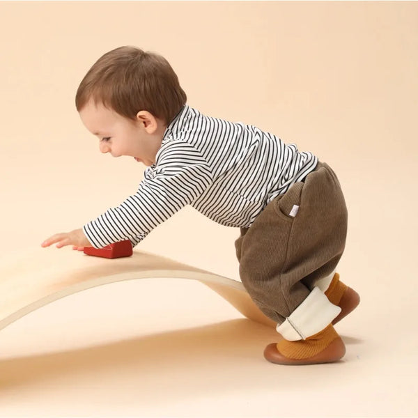 Toddler wearing sock shoes while leaning on a curved wooden play board.