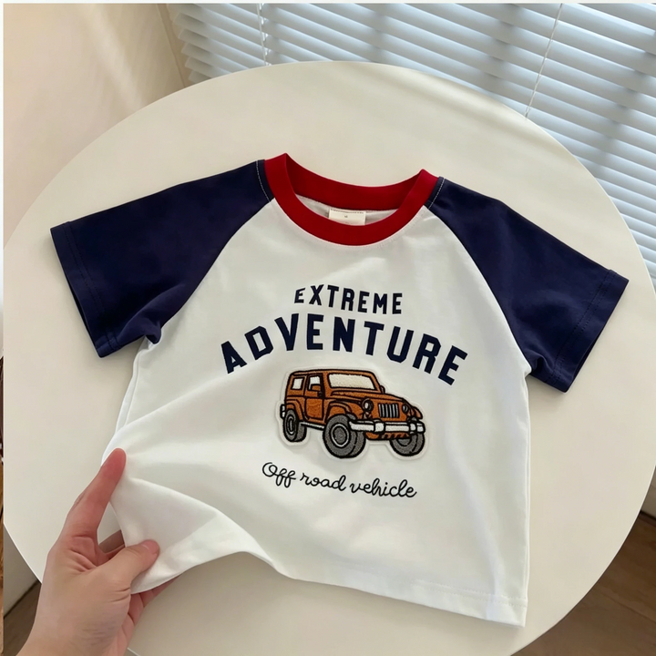 Truck graphic T-shirt with navy short sleeves and a red neckline laid flat on a round table
