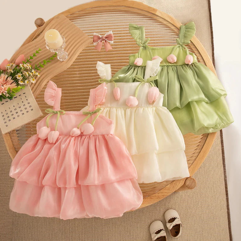 Pink, cream, and green tiered tulip dresses arranged on a woven chair