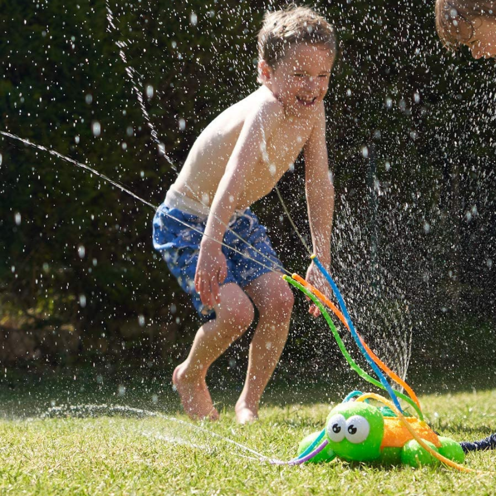 Child splashing beside a turtle sprinkler on the grass.