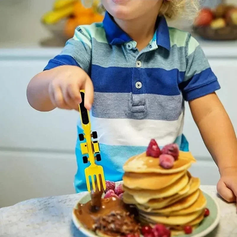 Child using a yellow construction-vehicle fork beside a stack of pancakes.