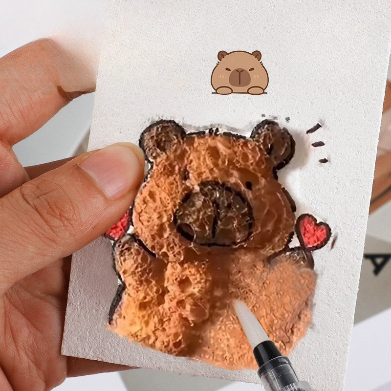 Water brush touching a textured brown bear design on a white sponge sheet