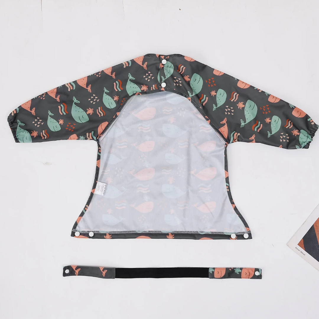 Reverse side of a whale-print long-sleeve bib laid flat with a separate strap