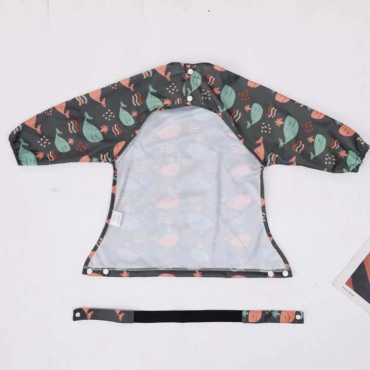 Reverse side of a whale-print long-sleeve bib laid flat with a separate strap
