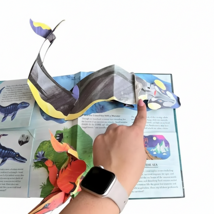 Hand pointing to a whale-shaped pop-up on an open illustrated book spread