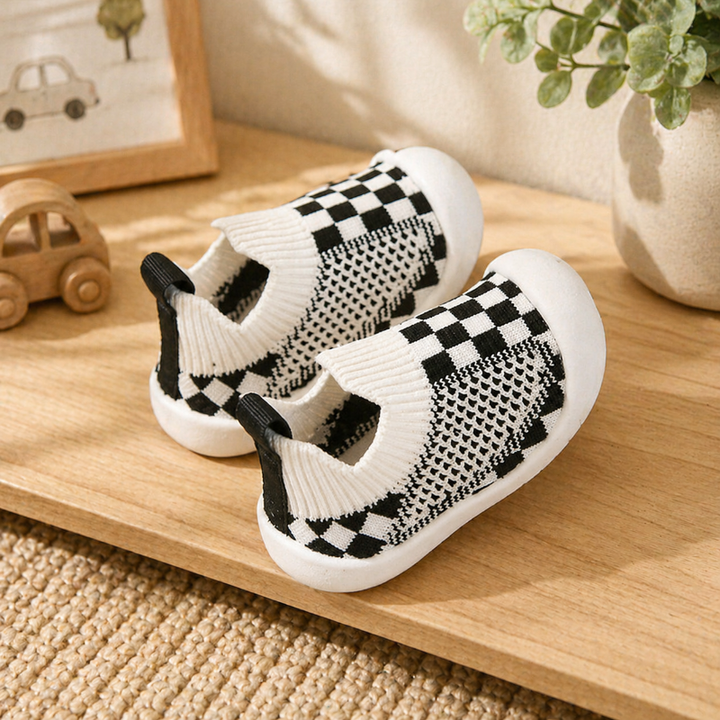 White and black checkerboard baby sock shoes with knit cuffs and heel pull tabs.