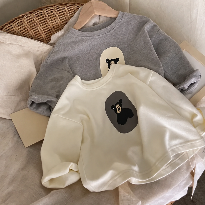 White and gray bear-print sweaters arranged together on a cushioned chair