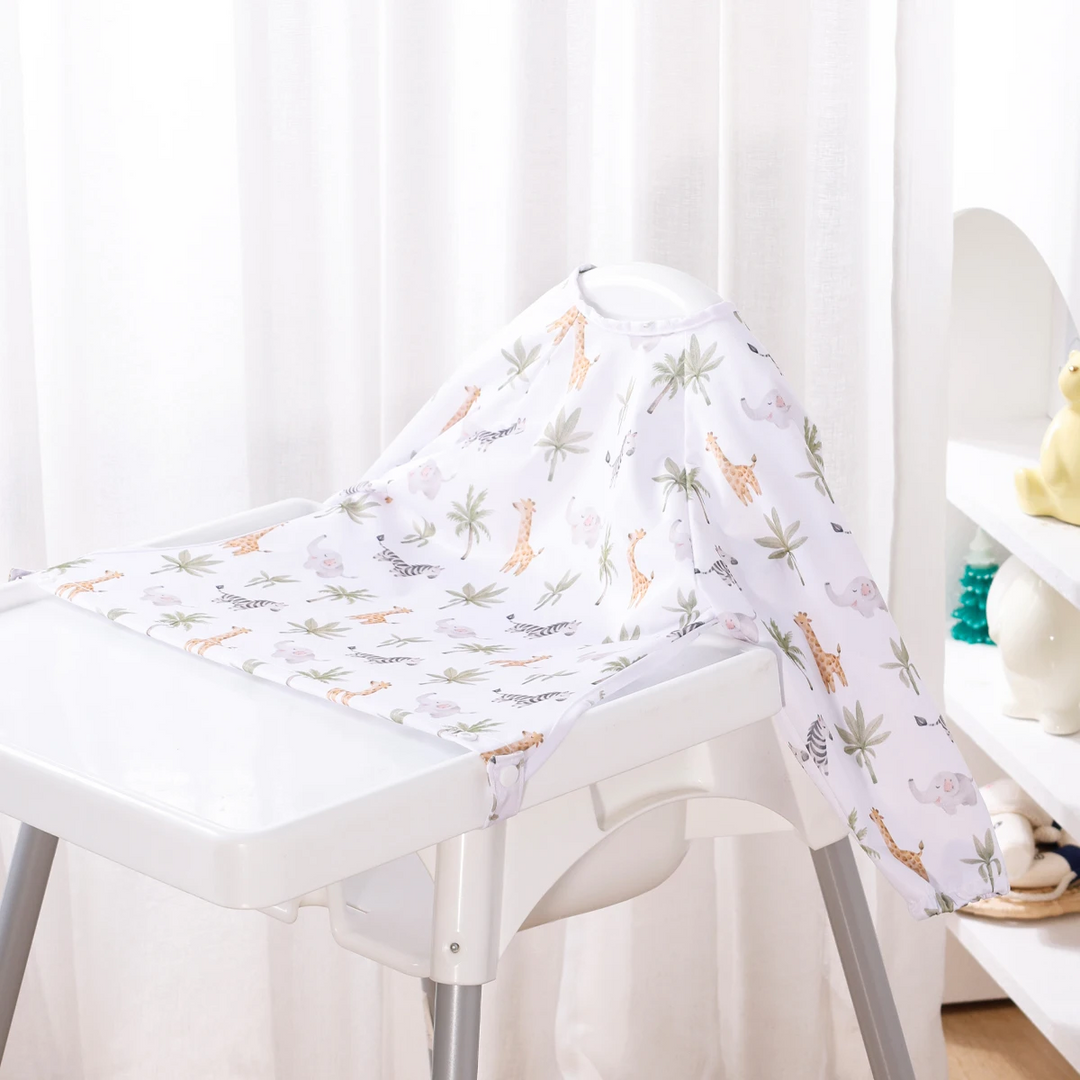 White long-sleeve baby bib with small animals and leafy branches on a high chair