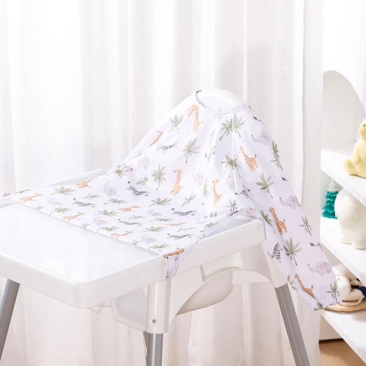 White long-sleeve baby bib with small animals and leafy branches on a high chair