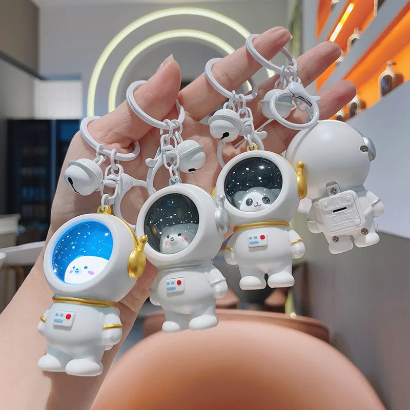 White astronaut keychains held together, showing front and back views and one blue-lit helmet