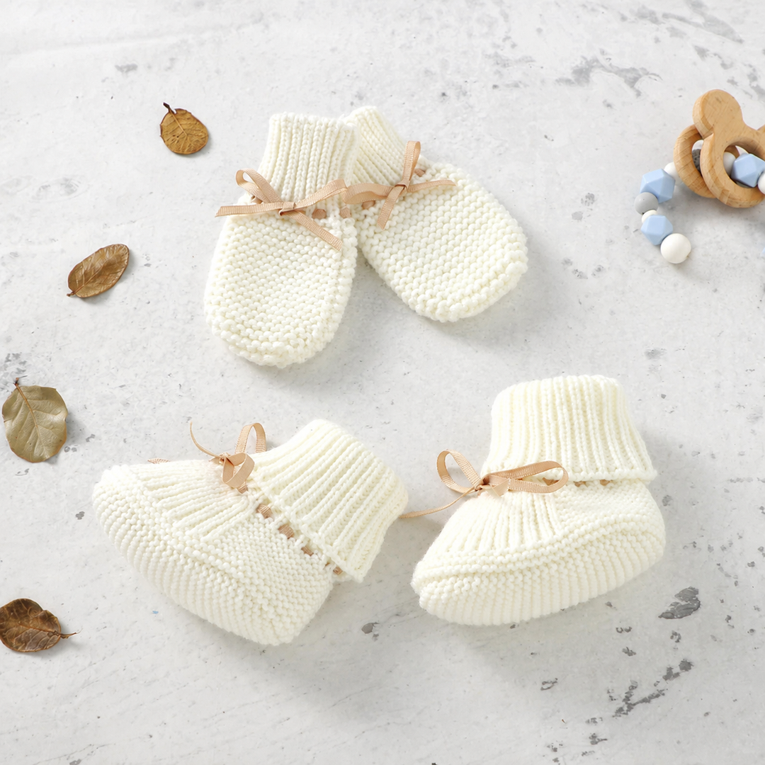 White knitted baby booties and matching mittens with beige bows