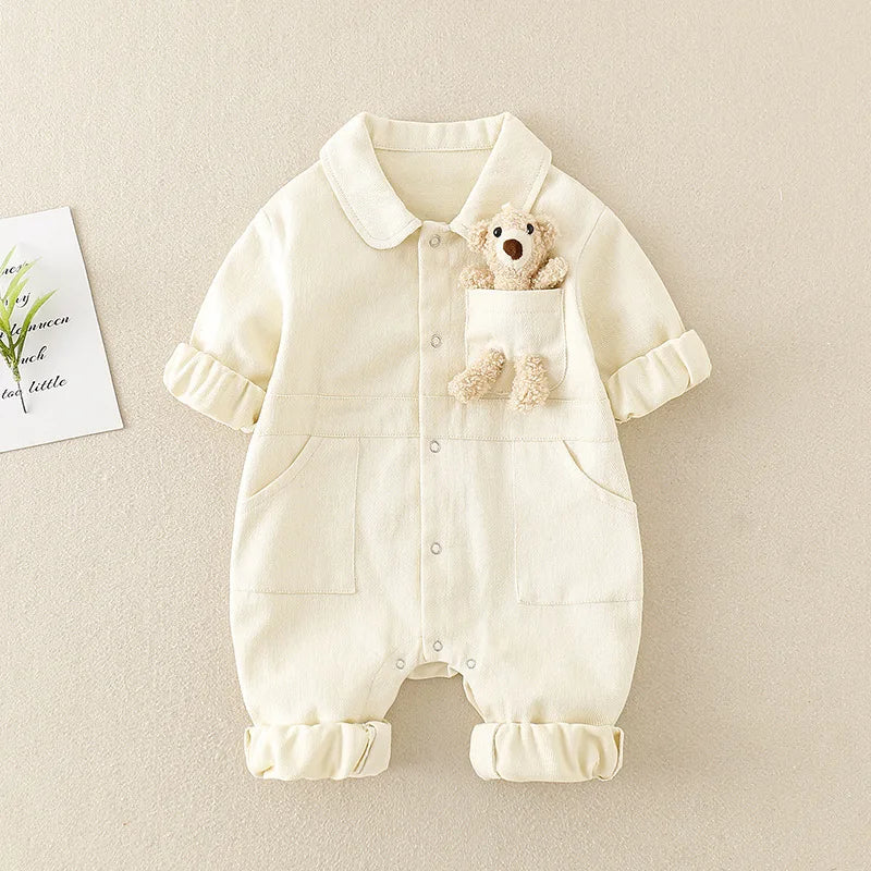 White baby jumpsuit showing the button front, large front pockets, and bear detail at the chest.