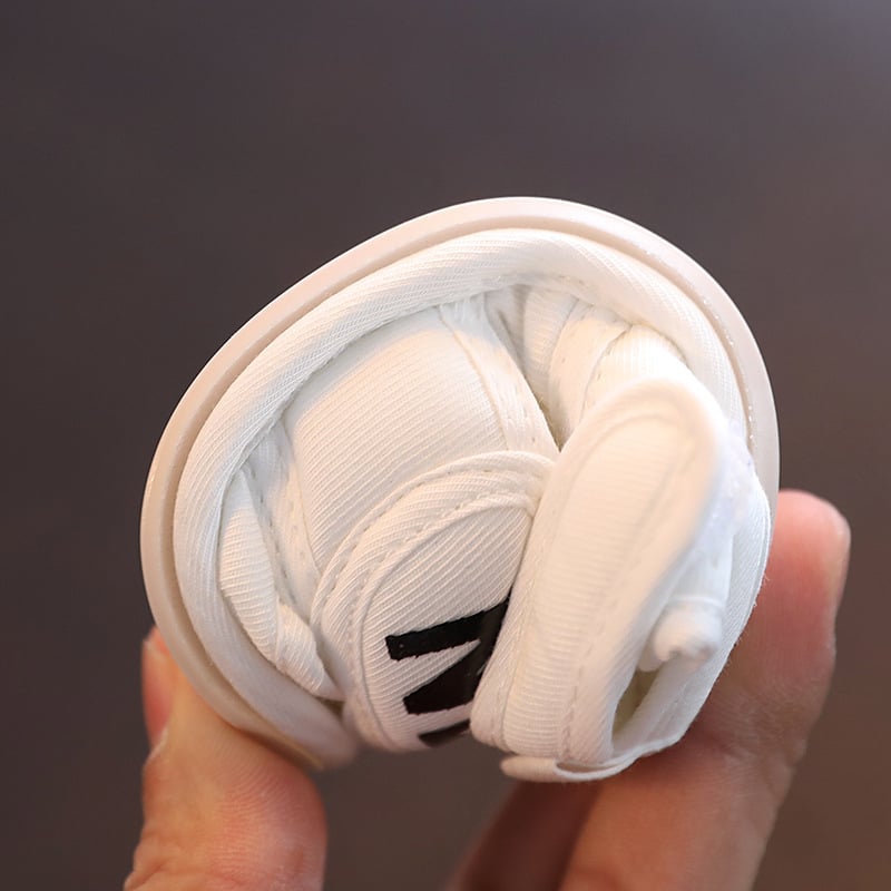 White baby sandal folded by hand to demonstrate its flexibility