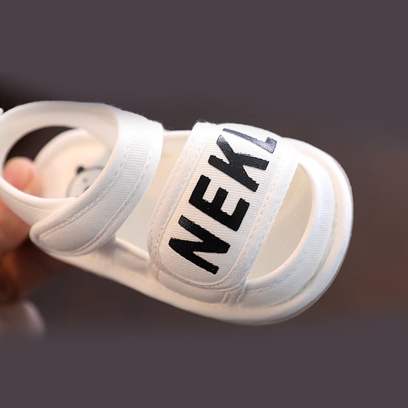 Close-up of a white baby sandal with a wide front strap and hook-and-loop ankle closure
