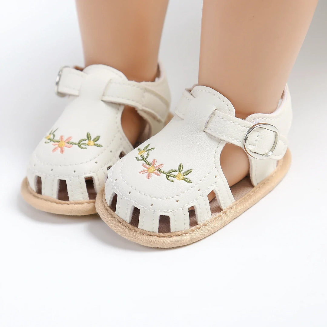 White floral baby sandals on mannequin feet, showing rounded toes and side openings
