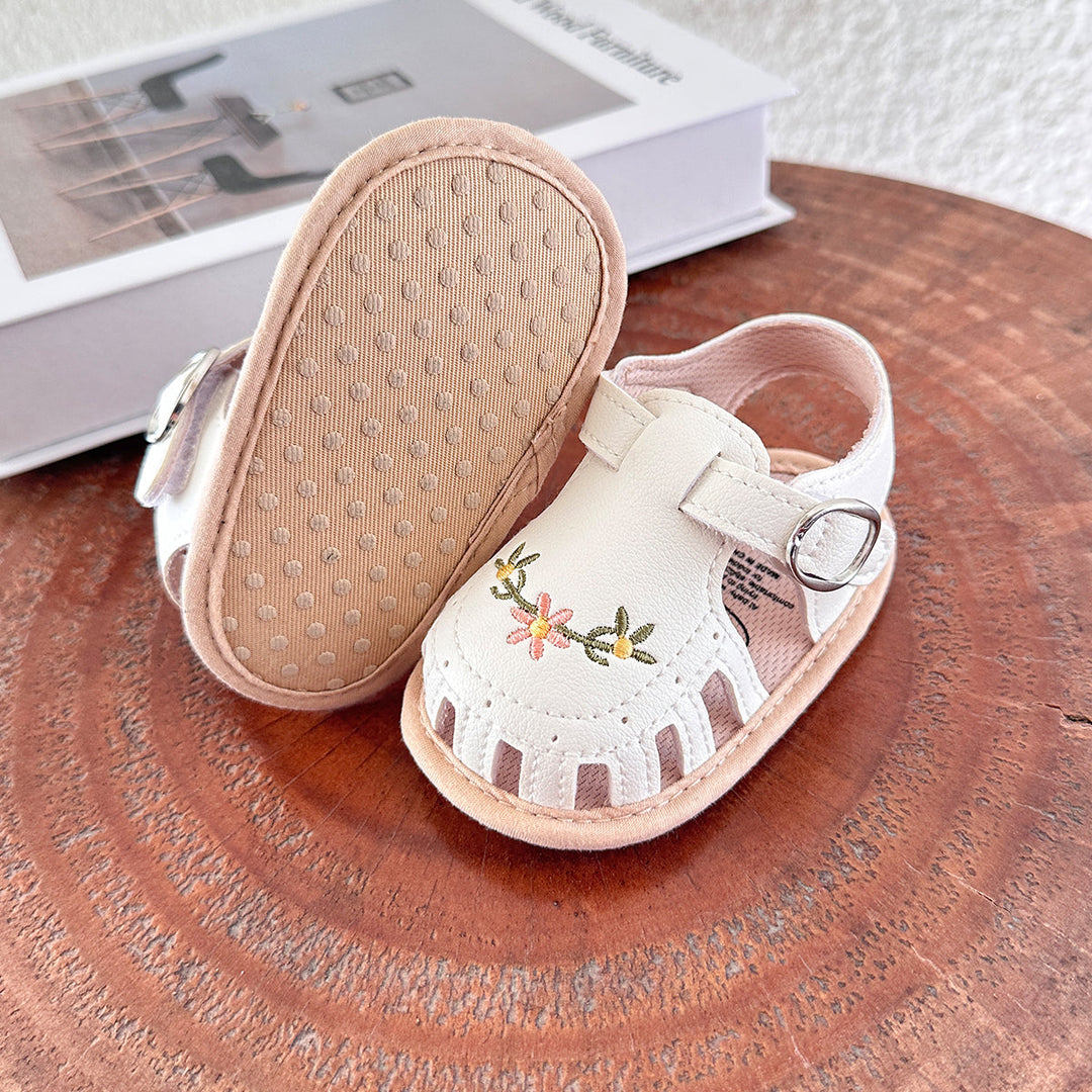 White embroidered baby sandals with one turned over to show the textured rubber sole