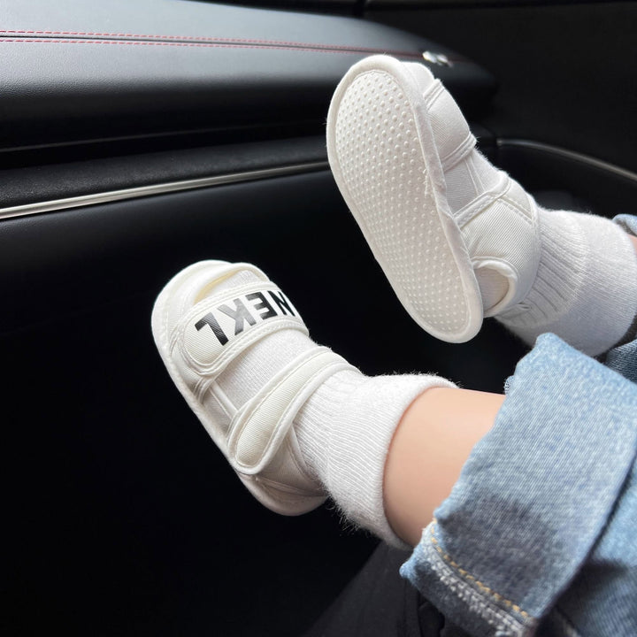 Baby wearing white sandals over socks, with one textured sole facing outward