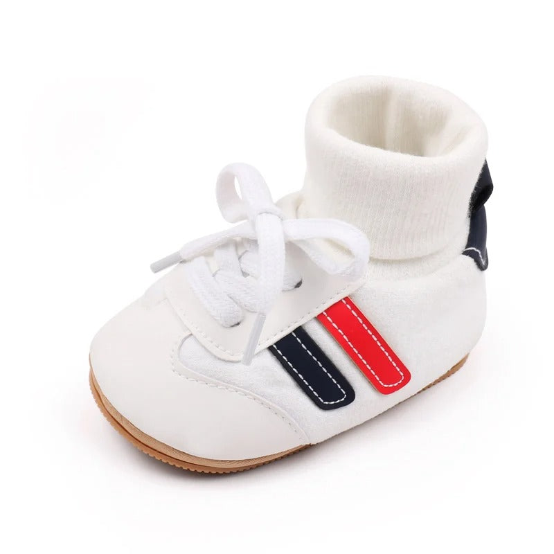White baby shoe with a ribbed ankle cuff, white laces, and red and navy side stripes