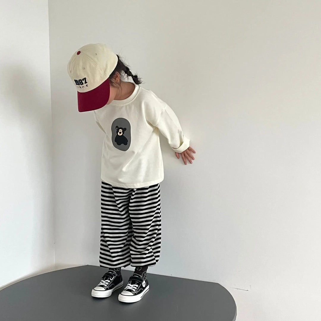 Child wearing a white bear-print sweater with striped pants and sneakers