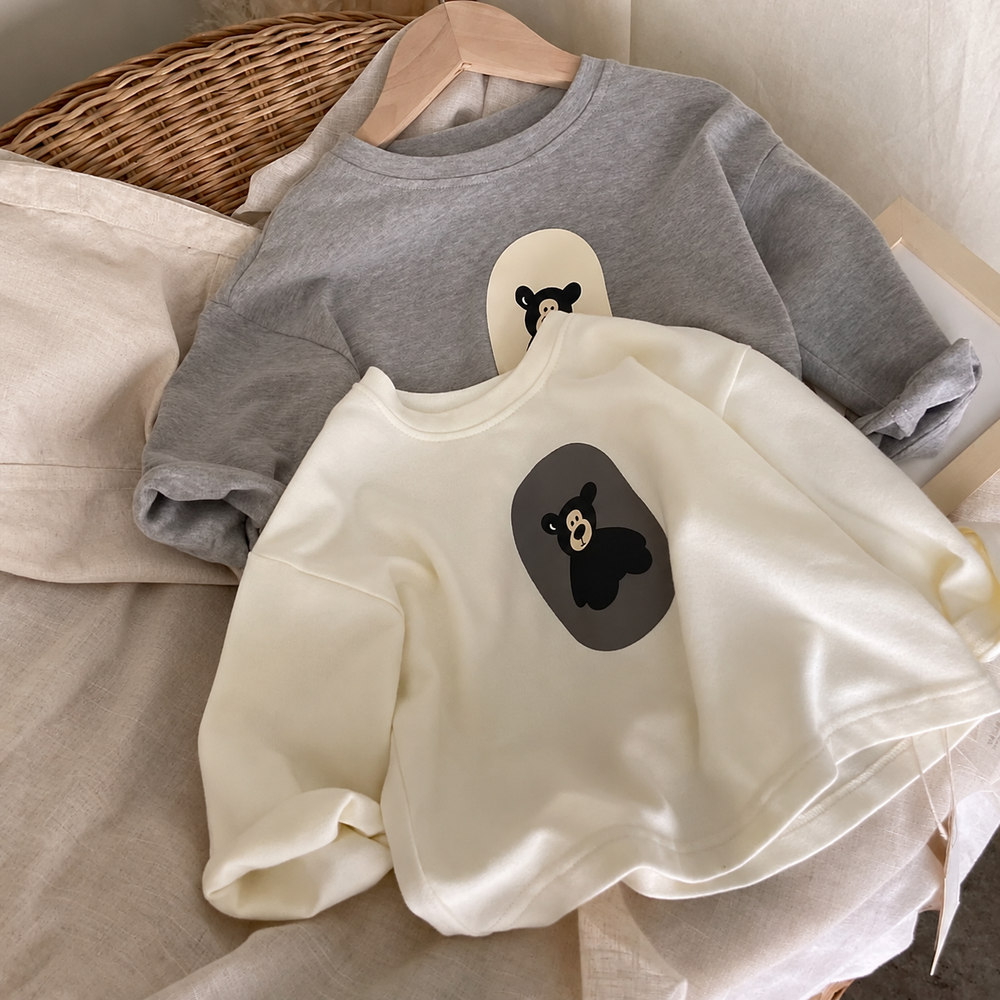 White bear-print sweater laid in front of the gray option, both with long sleeves and round necklines