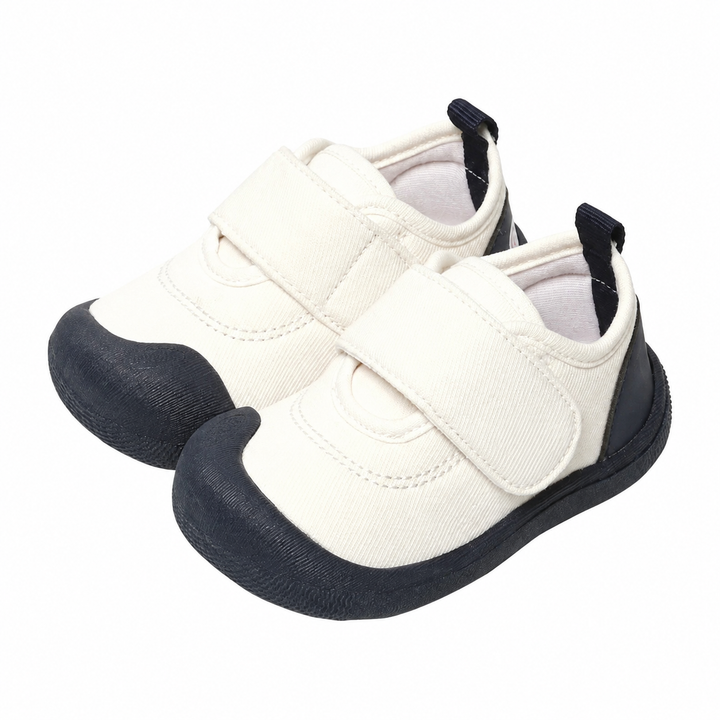 White canvas baby sneakers with black toe caps, black soles, and wide strap closures