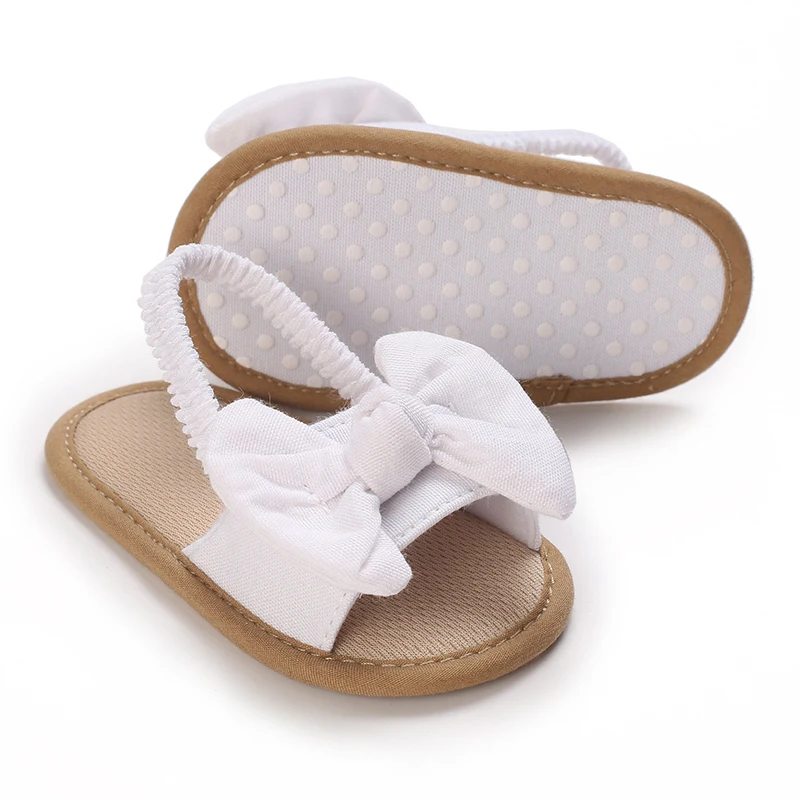 White bow baby sandals with one sandal turned to show its dotted sole