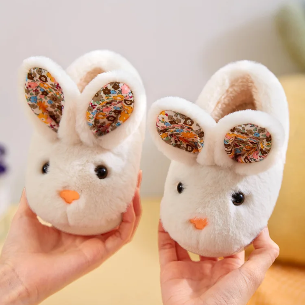 Pair of white bunny slippers held up to show their faces, floral ears, and openings
