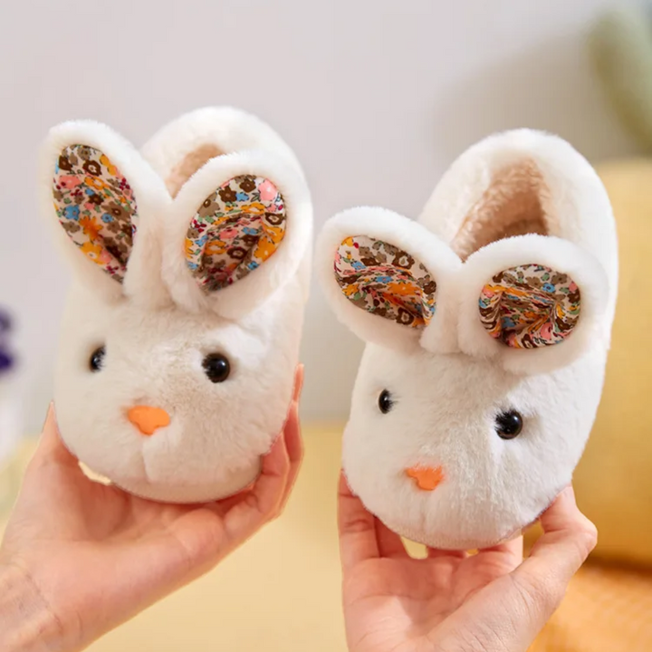 Pair of white bunny slippers held up to show their faces, floral ears, and openings