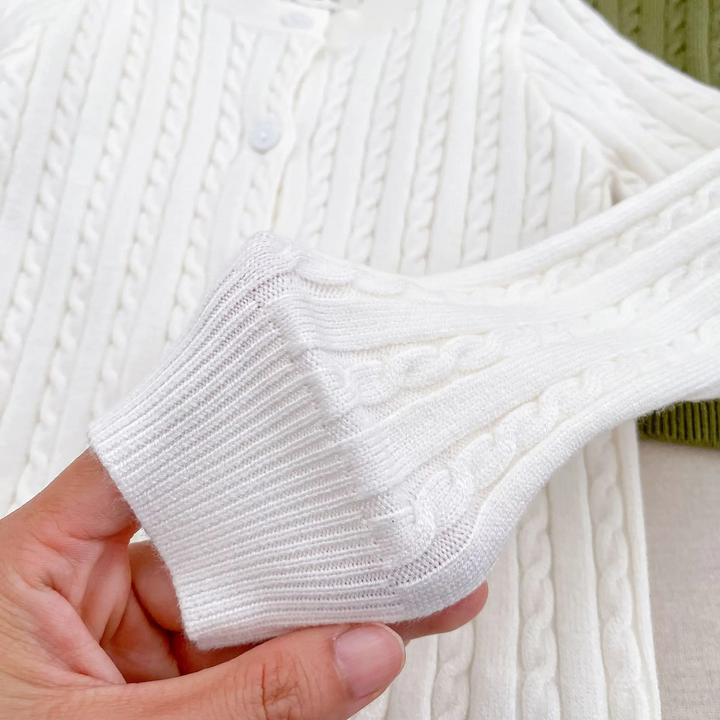 Hand holding the ribbed sleeve cuff of a white cable-knit cardigan