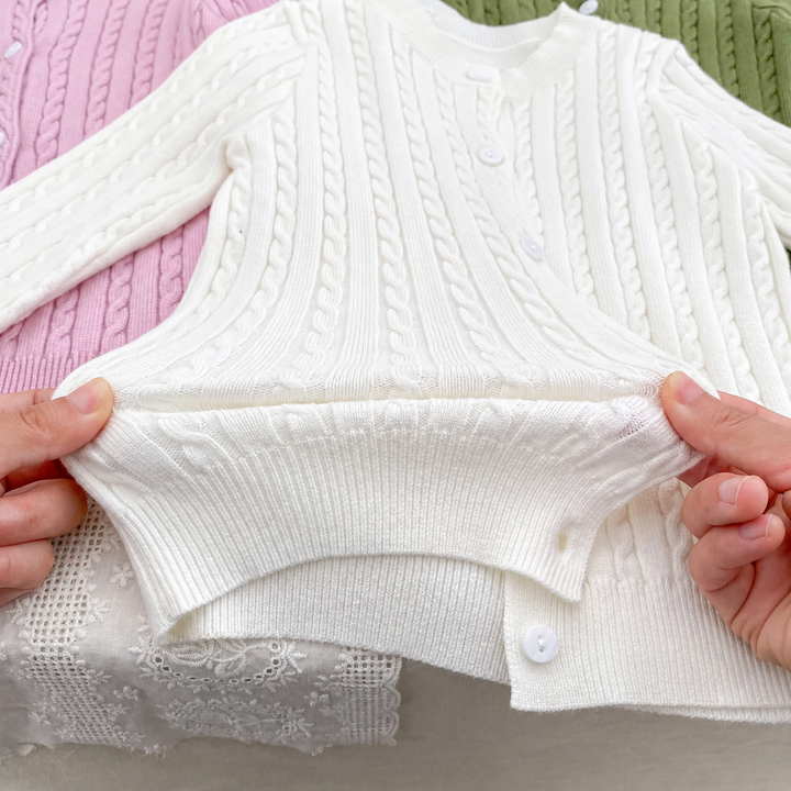 Hands holding the ribbed hem of a white cable-knit cardigan