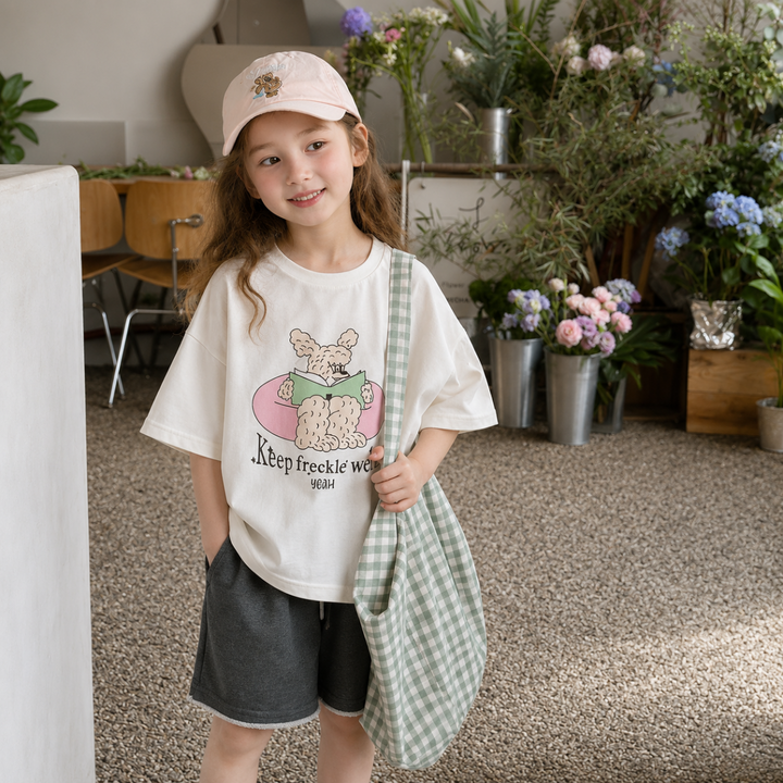 Girl wearing a white cartoon-print T-shirt with gray shorts and a green gingham bag