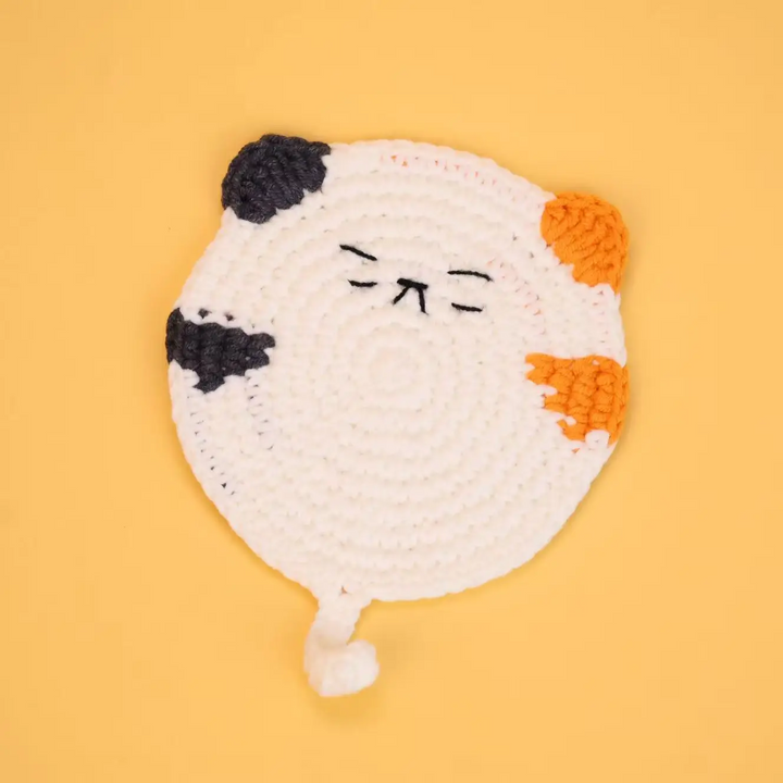 White cat coaster with orange and black patches, stitched whiskers, and a curled tail