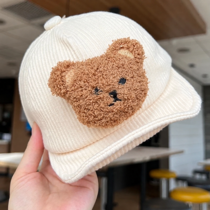 White corduroy baby cap held to show the textured brown bear face