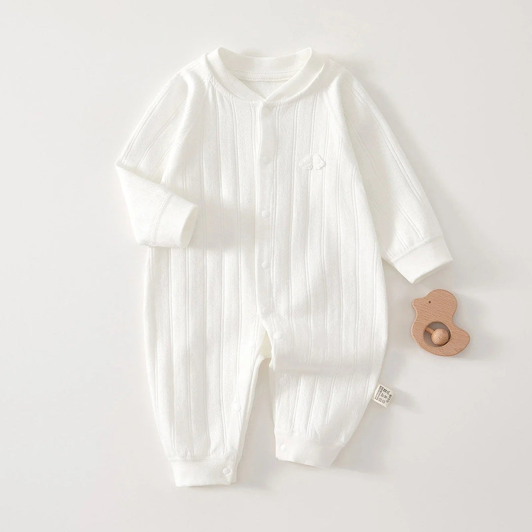 White cotton baby romper laid flat with a wooden toy beside it