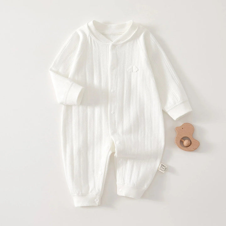 White cotton baby romper laid flat with a wooden toy beside it