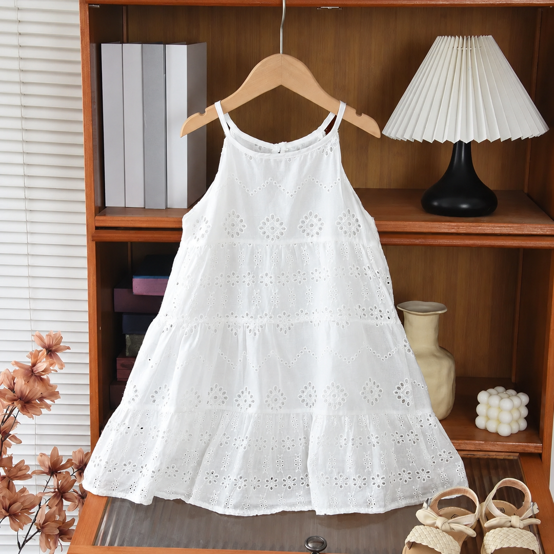 White cotton eyelet dress with narrow straps and a flared, tiered skirt on a wooden hanger