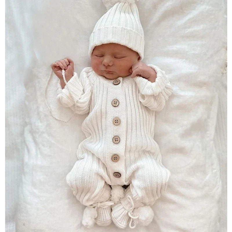 Sleeping baby wearing a white cotton-knit romper with a knit hat and booties