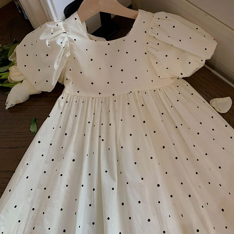 Front of the white dotted dress, showing its straight neckline, puff sleeves and gathered skirt.