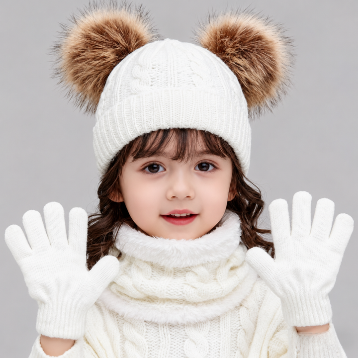 Child wearing a white double-pom-pom knit hat, matching scarf, and gloves