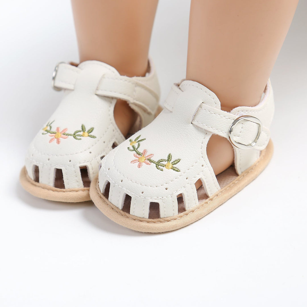 White baby sandals shown from the front with flower embroidery and adjustable straps