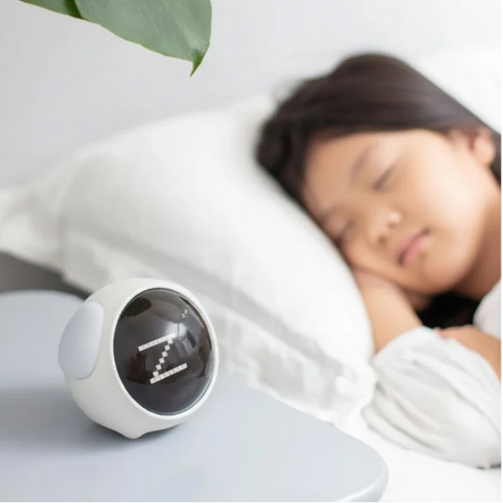 White expression alarm clock on a bedside table beside a sleeping child