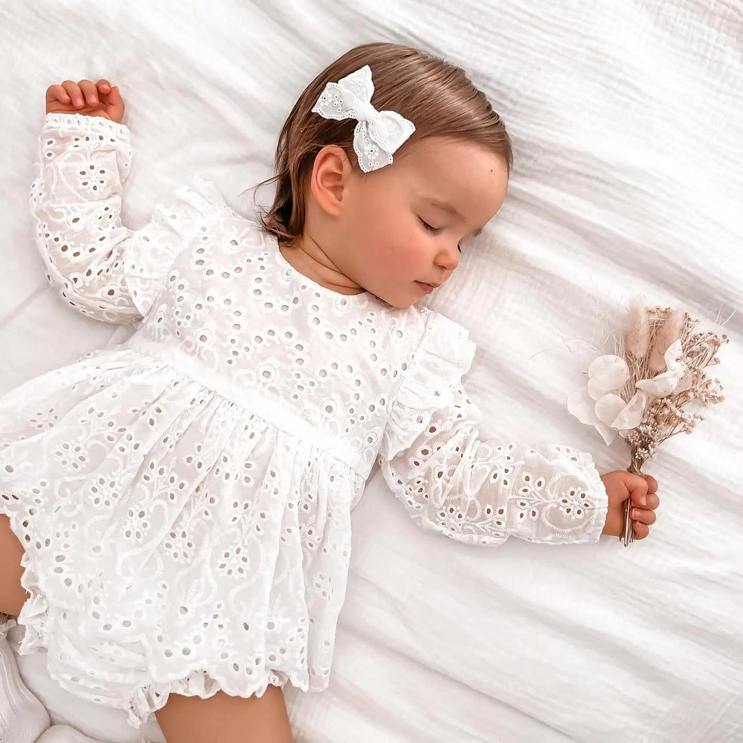 Baby wearing a white eyelet ruffle top and matching shorts while lying on a bed.