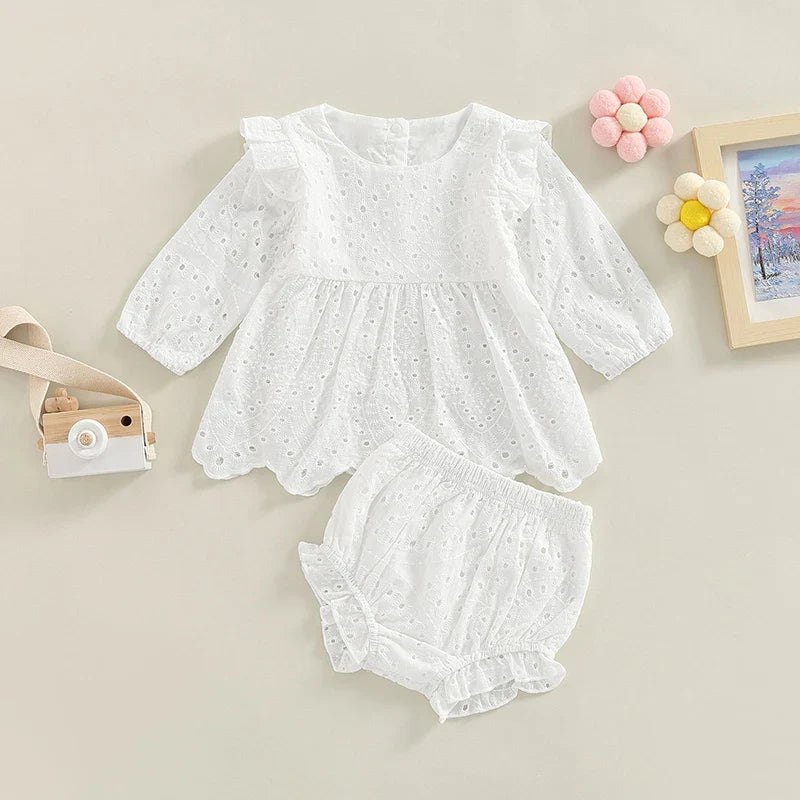White eyelet baby top with ruffled shoulders and matching shorts laid below.