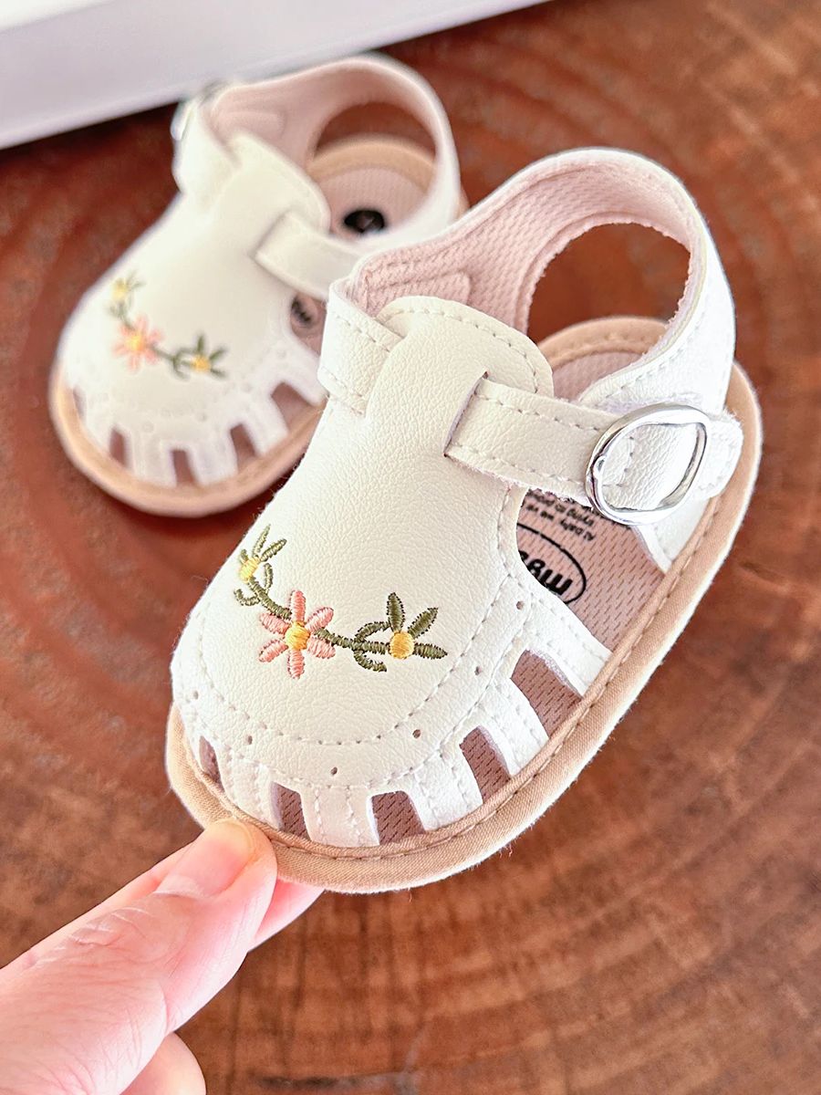 White floral baby sandal held at the toe beside its matching sandal