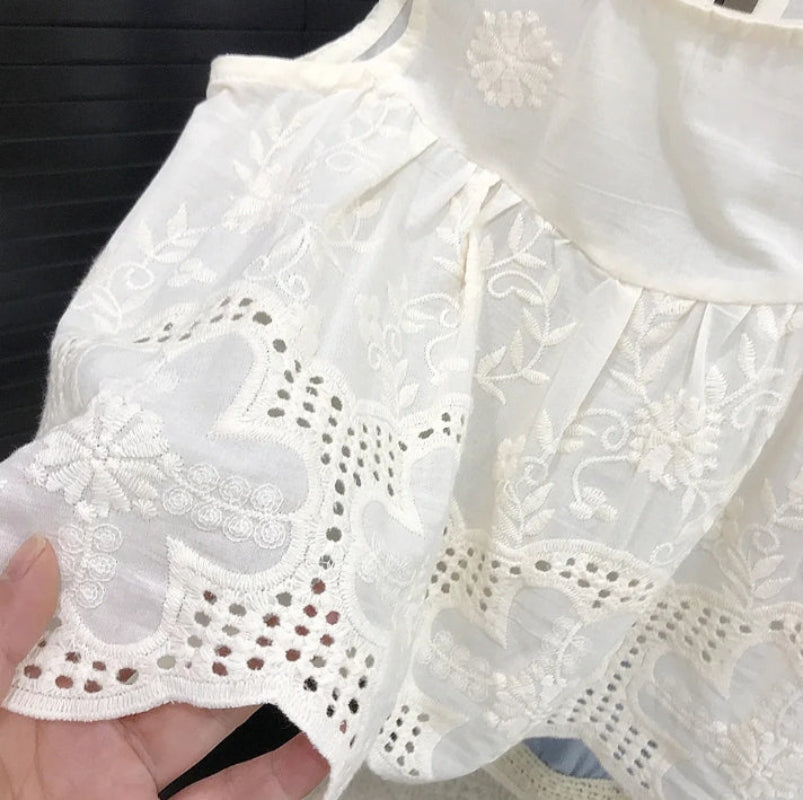 Close-up of floral embroidery and scalloped eyelet edging on a white sleeveless top