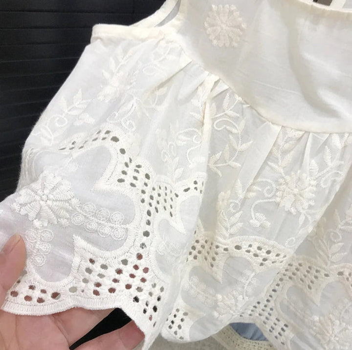 Close-up of floral embroidery and scalloped eyelet edging on a white sleeveless top